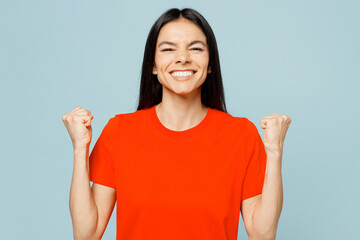 Young latin woman wear orange red t-shirt casual clothes doing winner gesture celebrate clenching...