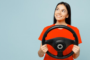 Young smiling happy minded dreamful latin woman wear orange red t-shirt casual clothes hold steering wheel driving car look aside isolated on plain pastel light blue cyan background Lifestyle concept