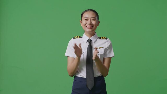 Asian Woman Pilot Smiling And Clapping Her Hands While Standing In The Green Screen Background Studio
