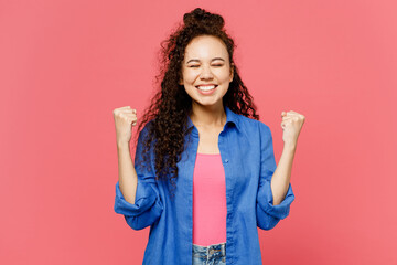 Young woman of African American ethnicity she wear blue shirt casual clothes doing winner gesture celebrate clenching fists say yes isolated on plain pastel pink background studio. Lifestyle concept.