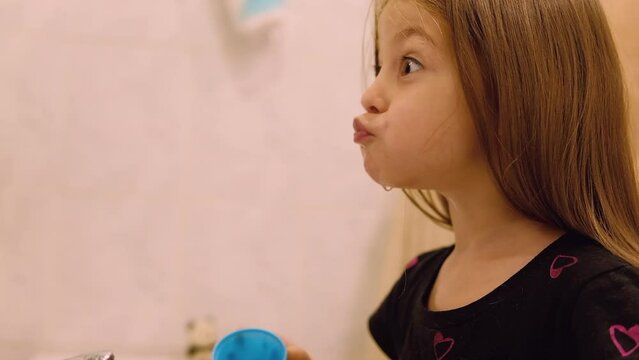 Little toddler girl one rinses her mouth and spits out water