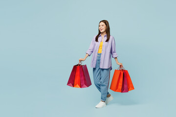 Fototapeta na wymiar Full body young woman wearing purple shirt yellow t-shirt casual clothes hold paper package bags after shopping isolated on plain light pastel blue cyan background. Black Friday sale buy day concept.