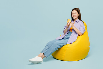 Full body young happy woman she wears purple shirt yellow t-shirt casual clothes sit in bag chair...
