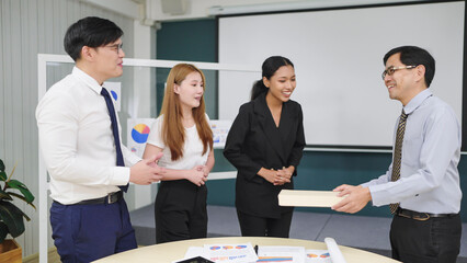Asian man manager giving gift box to group of Asian employees for celebrating succes new project at office. Friendships and celebration concept