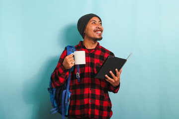 Young Asian male student takes a coffee break after lectures, isolated on blue background