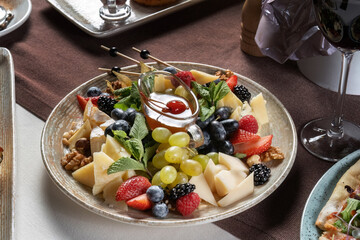 Cheese platter: variety of cheeses with fruits, nuts and berries. In the background are other dishes. Table set in a retoran. 45 view