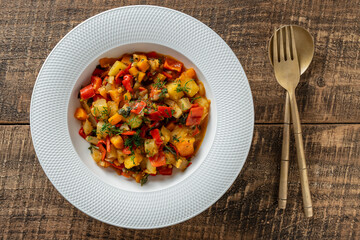 Vegetable stew in white plate on wooden background, closeup. Healthy food. Vegan dish.Top view