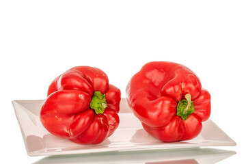 Two red sweet peppers on a ceramic white plate, macro, isolated on white background.