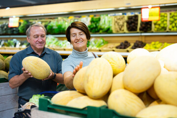 Fototapeta premium Senior married couple buy ripe melon in supermarket