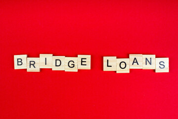 Bridge loans- word composed fromwooden blocks letters on red background, copy space for ad text.