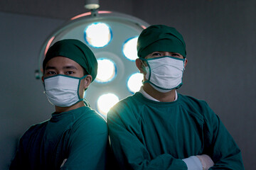 Fototapeta na wymiar Two professional surgeon doctor standing under bright light, using surgical equipment to do surgery at hospital operating room. Surgical team operating surgery patient, healthcare and medical.