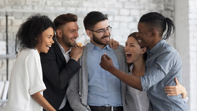 Overjoyed multiracial businesspeople hugging showing team support and unity, happy diverse multiethnic colleagues feel euphoric celebrate shared business victory or win, success, teamwork concept