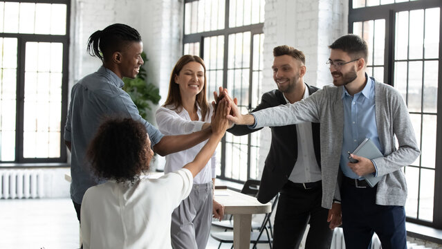 Overjoyed diverse multiethnic businesspeople give high five celebrated shared team victory or success, happy multiracial colleagues engaged in teambuilding activity at meeting, teamwork concept