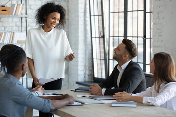 Happy diverse businesspeople sit at desk brainstorm discuss idea at team meeting in office, multiracial colleagues speak negotiate cooperate at group briefing, engaged in talk, collaboration concept