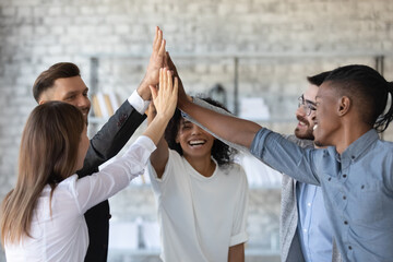 Overjoyed multiethnic businesspeople give high five engaged in teambuilding activity at meeting,...