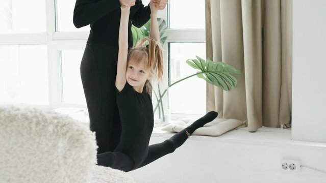 A gymnastics teacher helps young gymnastic girl stretching and do the splits