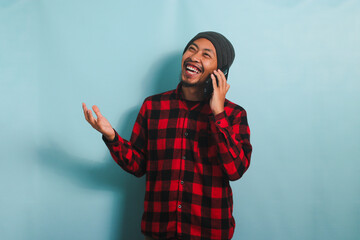 Happy Young Asian man is laughing hearing funny jokes on his phone call, isolated on blue background