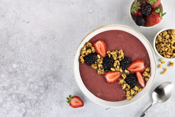 Obraz na płótnie Canvas Smoothie bowl with strawberries, blackberries and granola on a gray background. Healthy breakfast. Top view. Copy space.