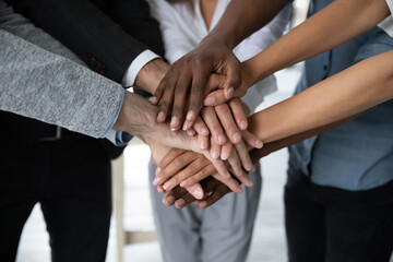 Close up of multiracial colleagues stack hands in pile engaged in teambuilding activity in office together, motivated diverse coworkers have business training at meeting, show unity, teamwork concept