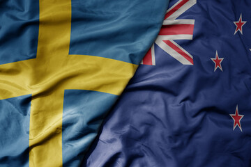 big waving national colorful flag of sweden and national flag of new zealand .
