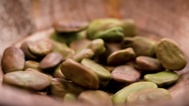 Raw fava (faba) beans falling into a wooden bowl in slow motion close up