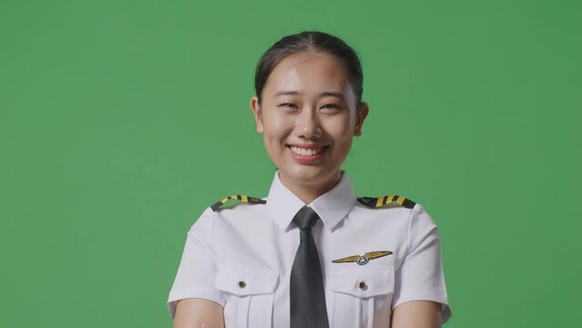 Close Up Of Asian Woman Pilot Smiling And Crossing Her Arms To Camera While Standing In The Green Screen Background Studio
