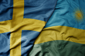 big waving national colorful flag of sweden and national flag of rwanda .