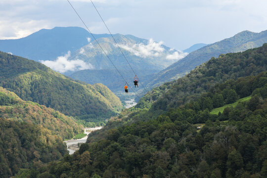 Two tourists going down on a zipline, against the backdrop of a picturesque mountain landscape. Sochi, Solokhaul, Russia.