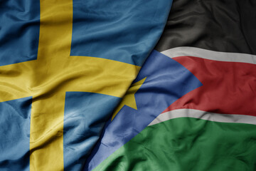 big waving national colorful flag of sweden and national flag of south sudan .