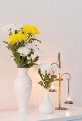 chrysanthemums flowers in vases and burning candles on white interior