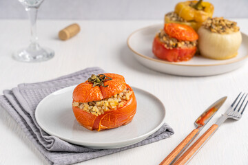 Homemade healthy tomato stuffed with rice and baked until soft served on plate on towel on white wooden table with tableware and glass of wine as part of gemista greek cuisine made of vegetables