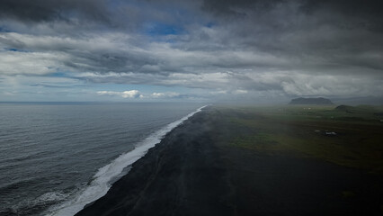 Aerial view of black sand beach Reynisfjara with ocean under majestic cloudy sky near VIK and Golden Circle in Iceland