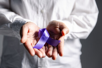 Woman with purple ribbon on palm background, closeup with space for text. Domestic violence awareness. Purple Ribbon for supporting people living. Healthcare and World cancer day concept.
