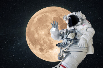Space man astronaut greets and waves his hand in space on a background of amazing full moon. Space...