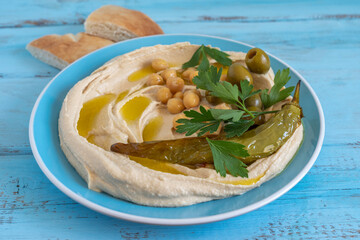 Fresh parsley and baked hot pepper on freshly prepared hummus in ceramic plate.