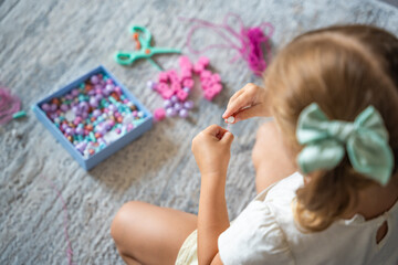 Obraz na płótnie Canvas Little girl making wooden beads bracelet at home living room. Children's creativity and the development of fine motor skills