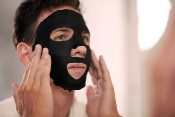 Face of young man applying charcoal sheet mask