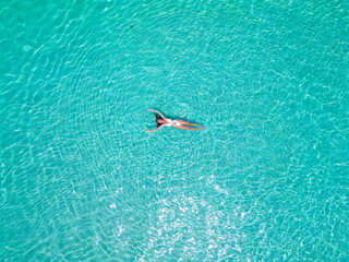 Top aerial drone view of a girl in a white swimsuit relaxing, swimming, and sunbathing lying on the sparkling clear blu water in the ocean in the Maldives © Alona