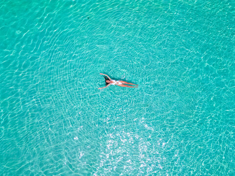 Top aerial drone view of a girl in a white swimsuit relaxing, swimming, and sunbathing lying on the sparkling clear blu water in the ocean in the Maldives - Powered by Adobe