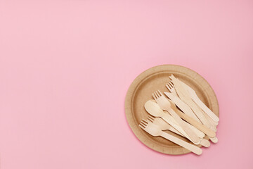 wooden disposable cutlery on a disposable paper plate on a pink background with copy space