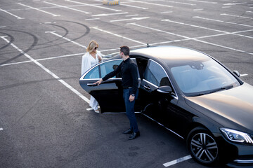 Chauffeur helps a businesswoman to get out of a car on parking lot, view from above. Concept of transportation and business transfer - 646013576