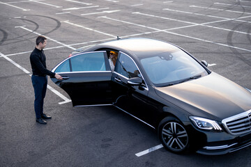 Chauffeur helps a businesswoman to get out of a car on parking lot, view from above. Concept of...
