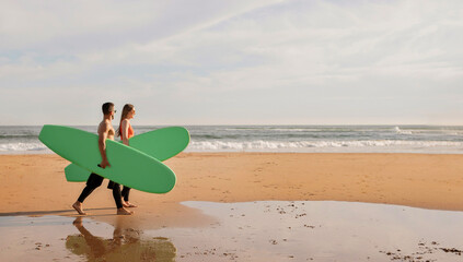 Fototapeta na wymiar Happy young surfers couple with surfboards walking along the beach