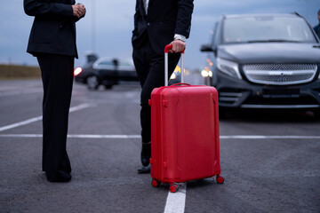 Business couple standing with a suitcase on parking lot, arrived by luxury taxi. Cropeed view with no face. Concept of transportation and business trips - 646016102