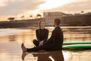 Happy Young Couple Relaxing On The Beach After Surfing Together