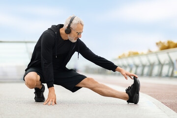 Determined elderly man stretching body, have outdoor workout