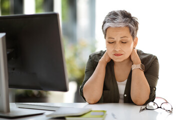 Tired woman sitting at workplace with closed eyes, rubbing neck