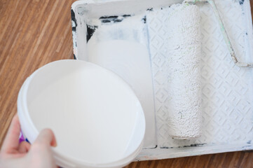 Worker pours white paint into a tray.