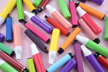 Set of multicolor disposable electronic cigarettes on a pink background.