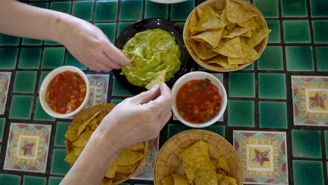 Family hands eating Mexican food corn nachos dipping salsa and avocado guacamole sauce